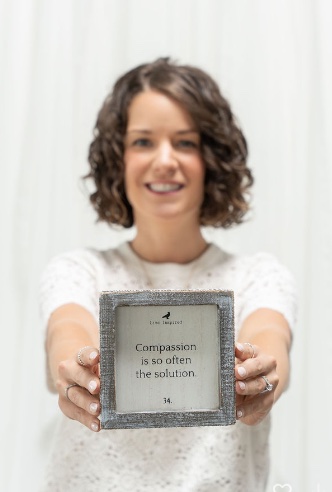Holding a small framed sign that reads: compassion is so often the solution
