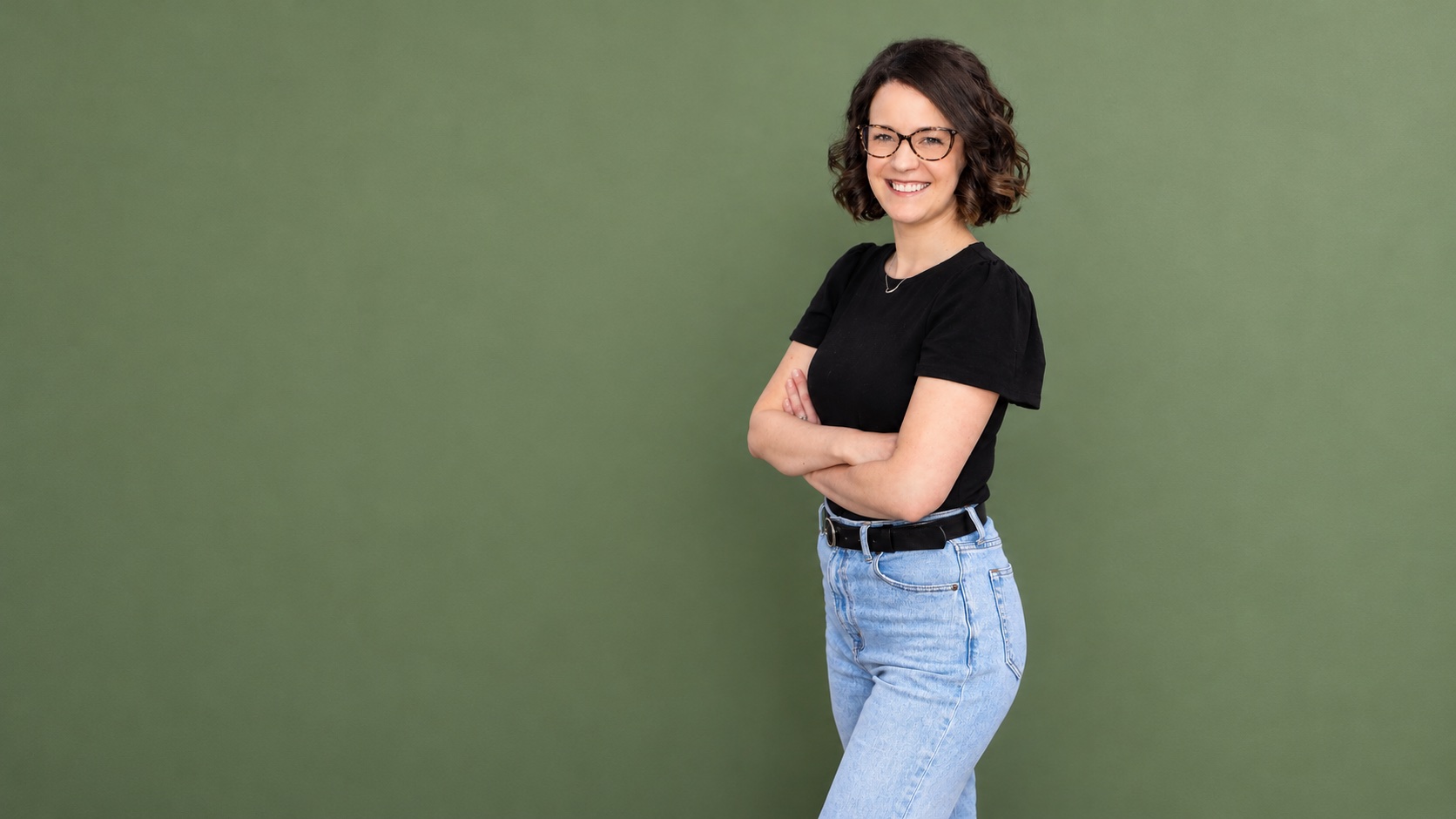 Smiling therapist with arms crossed on a sage green backdrop